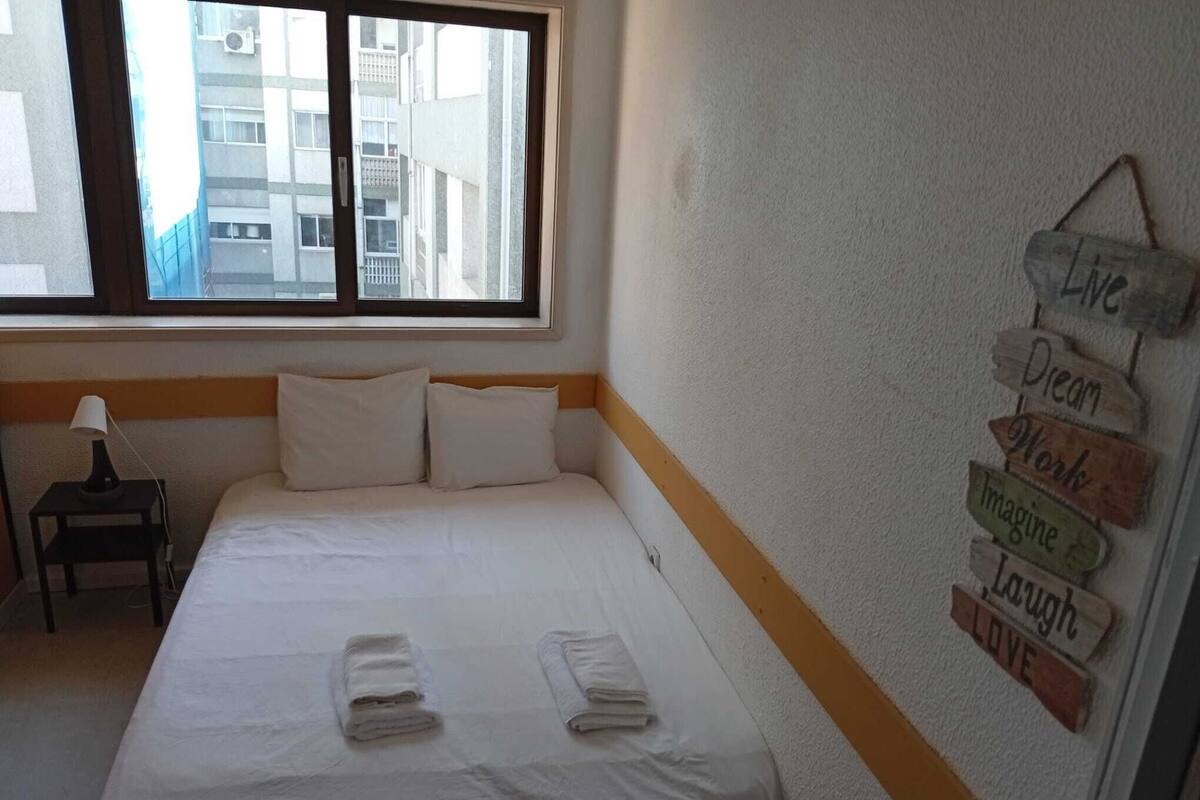 A hotel room with a bed, a nightstand, a window, and motivational wall decor.