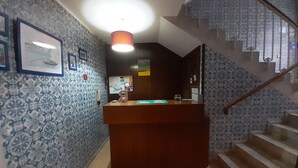 A reception desk with patterned wallpaper, a staircase with a railing, and a ceiling light fixture. - Porto Central Hostel (Porto)