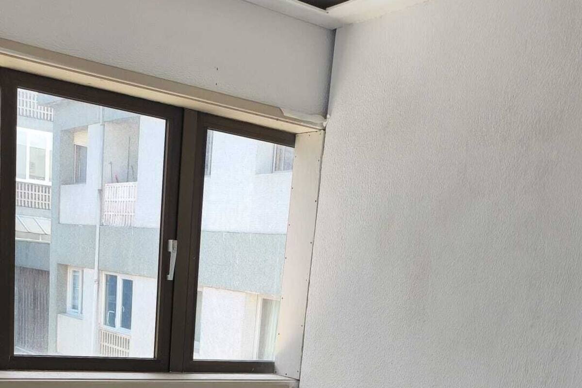 A single-bed room with a window, white walls, and a tiled floor.