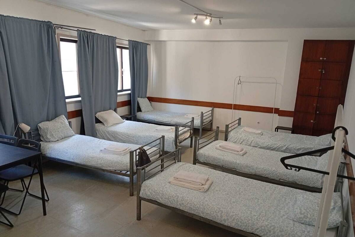 A dormitory room with four single beds, a desk, and a chair.