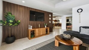 Un salon moderne avec un téléviseur à écran plat, une console en bois, une grande plante en pot, un canapé foncé et une table basse ronde.