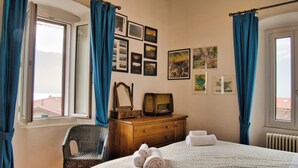 Une chambre d’hôtel avec un lit, une commode en bois, une chaise et une fenêtre avec des rideaux.