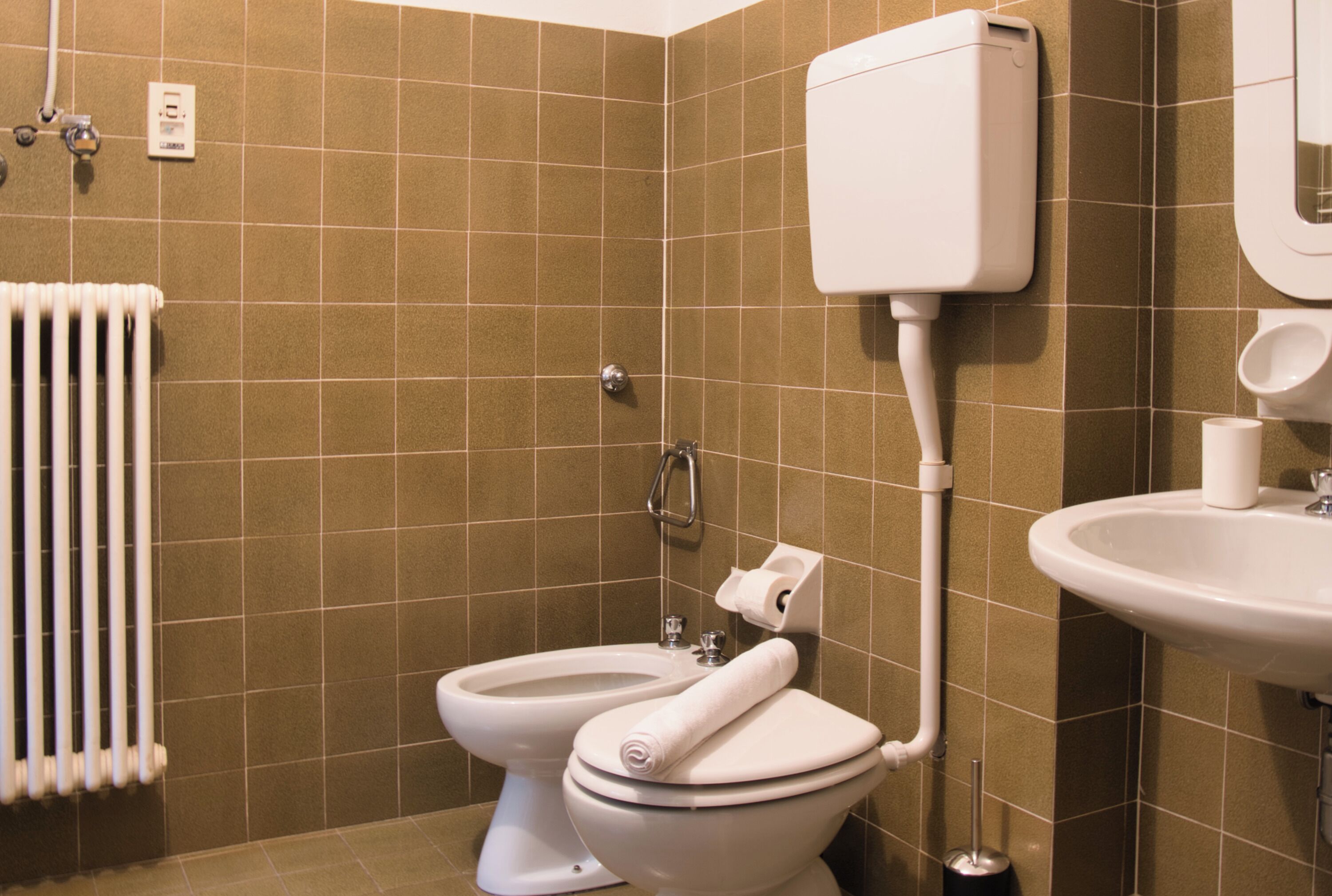 Une salle de bain avec deux toilettes, un lavabo, un porte-rouleau de papier toilette et un radiateur.