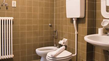Une salle de bain avec deux toilettes, un lavabo, un porte-rouleau de papier toilette et un radiateur.