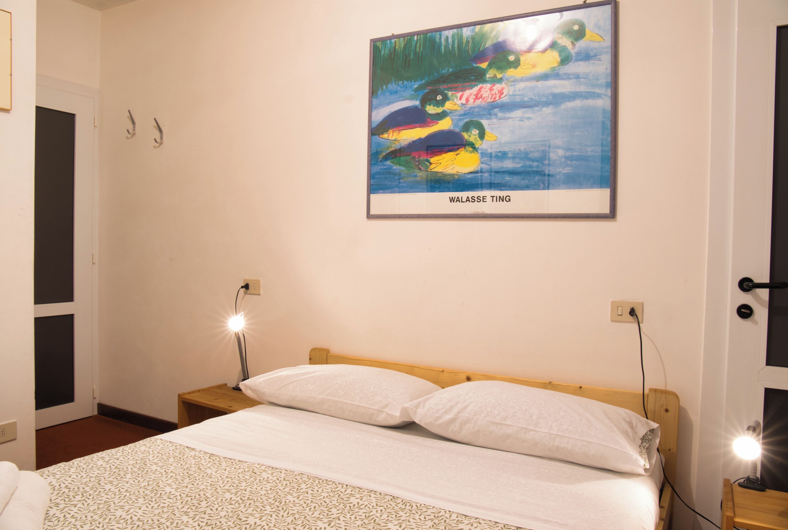 Un dormitorio con una cama, dos mesitas de noche, un cuadro en la pared y una puerta.