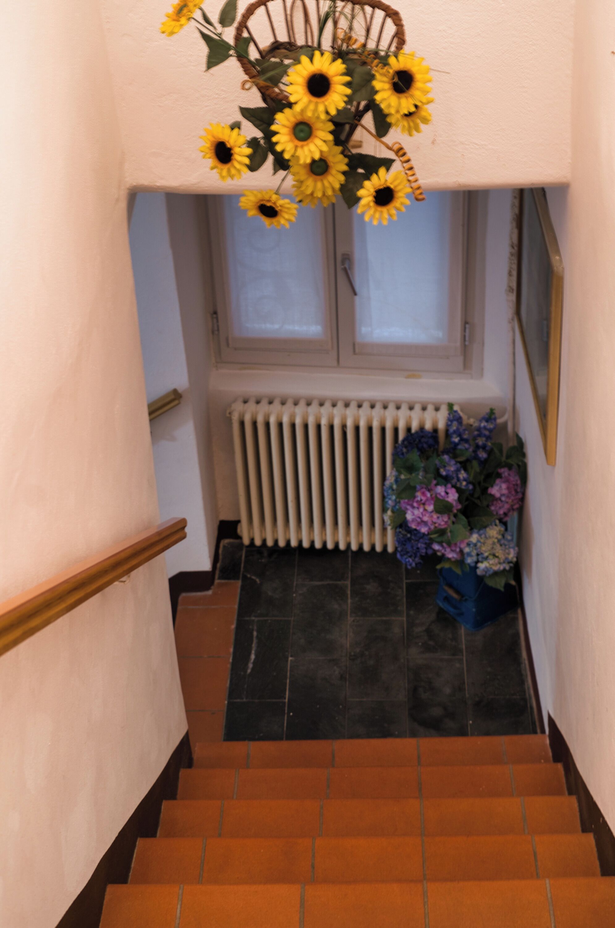 Un escalier avec un radiateur, une fenêtre et un vase rempli de tournesols.