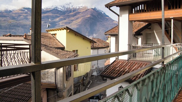 Un barrio residencial con montañas al fondo, con casas de techo de teja y un balcón con barandilla de metal.