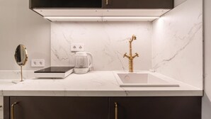 Eine moderne Küche mit weißer Arbeitsplatte, dunklen Schränken, einem goldenen Wasserhahn, einer Kaffeemaschine und einer Waage.