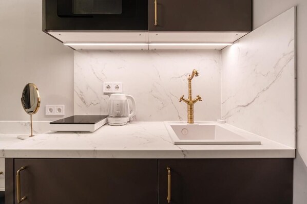 A modern kitchen with a white countertop, dark cabinets, a gold faucet, a coffee maker, and a scale. - Arany Boutique Residence by BQA (Budapest)