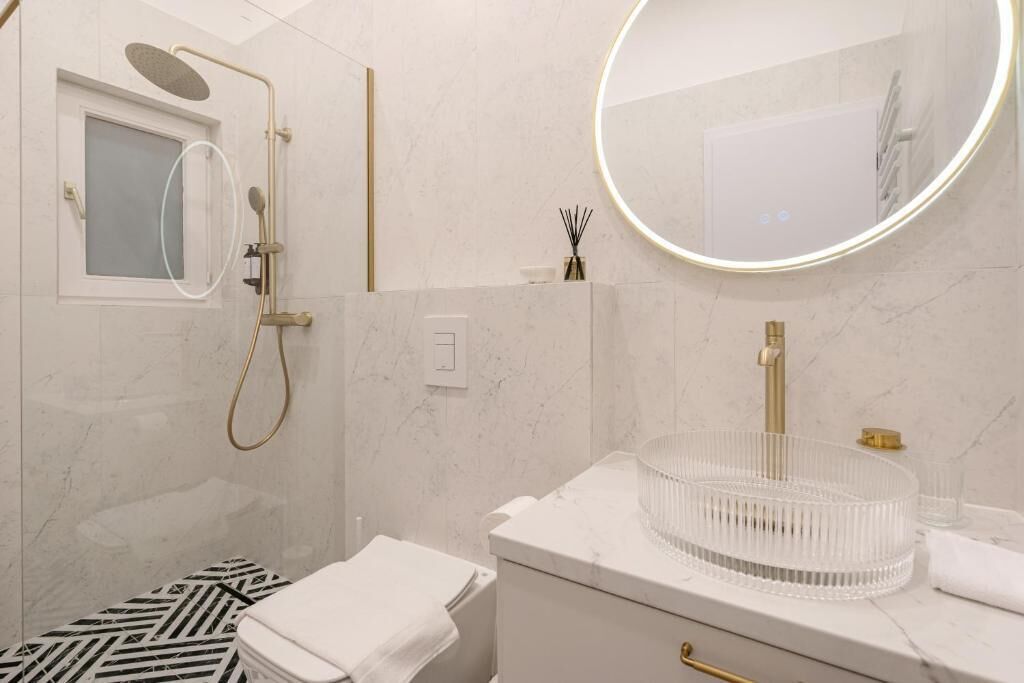 A modern bathroom with a shower, a toilet, and a sink with a round mirror.
