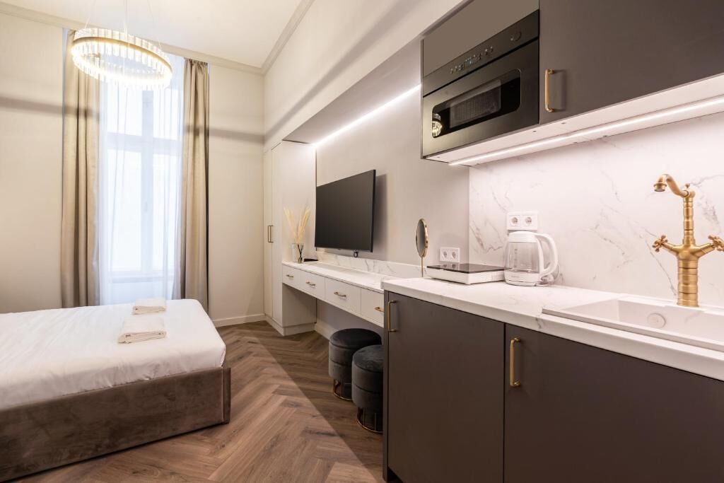 A modern hotel room with a bed, a TV, a kitchen area with a microwave, and a coffee maker.