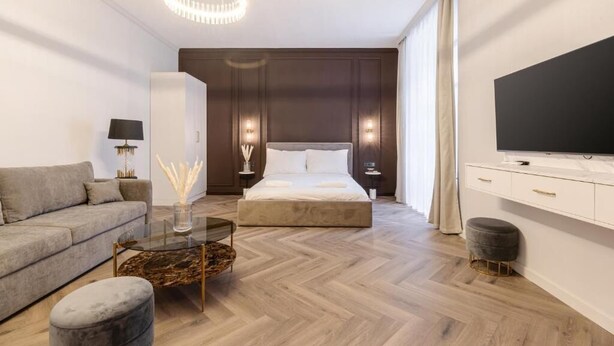Ein modernes Hotelzimmer mit einem großen Bett, einer Couch, einem Glastisch und einem Fernseher auf einer weißen Kommode.