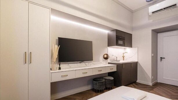 Ein modernes Hotelzimmer mit großem Kleiderschrank, Flachbildfernseher, Marmorplatte und einem Bett mit weißer Bettdecke.