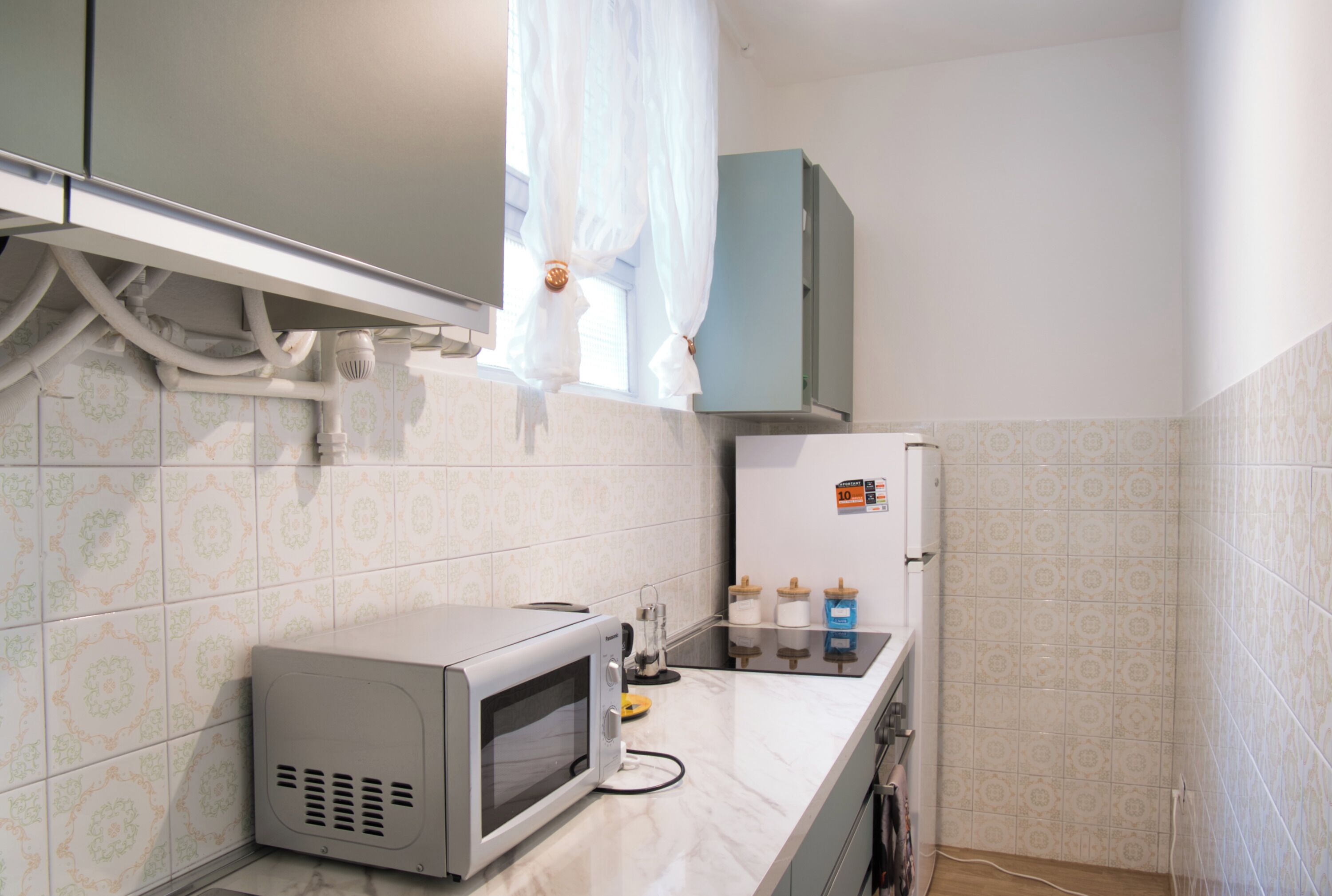 Una cocina compacta con microondas, un refrigerador pequeño y una ventana con cortina.