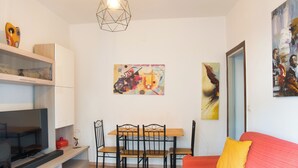 Un soggiorno moderno con televisore, tavolo da pranzo in legno, sedie, un divano rosso e opere d'arte alle pareti.