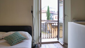 Ein Hotelzimmer mit Bett, einem gemusterten Kissen, einem Fenster mit Blick auf Gebäude und einer Tür, die nach draußen führt.