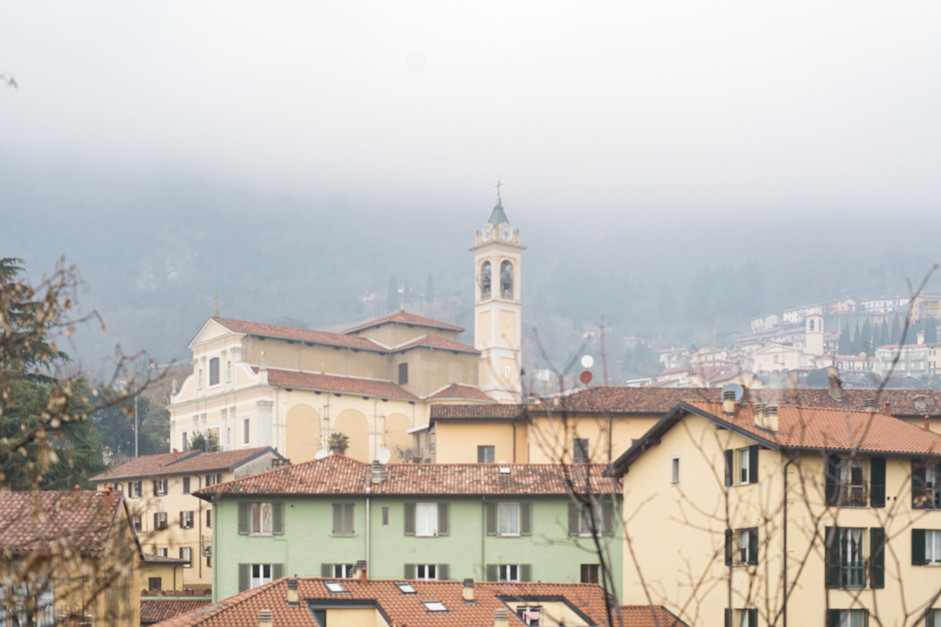 Una città storica con un campanile imponente, edifici tradizionali e uno sfondo collinare.