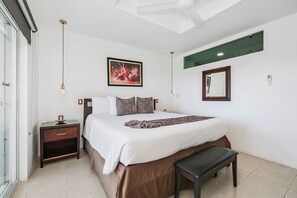 A bedroom with a bed, bedside table, bench, ceiling fan, wall-mounted mirror, and artwork. - Oceanfront Penthouse | Private Hot Tub | Private Pier | Downtown (Cozumel)
