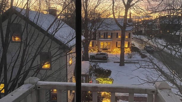 A view from a window overlooking a snow-covered street at dusk with houses and a car visible. - Little Downtown Apt with Beautiful Window View (Brunswick)