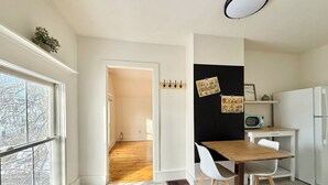 A modern kitchen with a wooden dining table, white chairs, a blackboard with notes, and a vintage microwave. - Little Downtown Apt with Beautiful Window View (Brunswick)