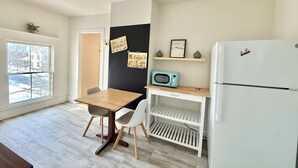 A compact kitchen with a wooden table, white chairs, a white refrigerator, a microwave, and a blackboard with notes. - Little Downtown Apt with Beautiful Window View (Brunswick)