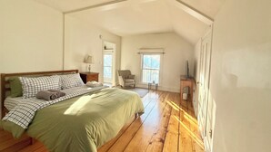 A bedroom with a large bed, wooden flooring, a chair, a small table, and a television. - Little Downtown Apt with Beautiful Window View (Brunswick)