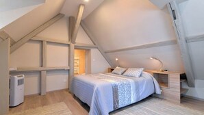Ein Schlafzimmer mit schräg verlaufender Decke, einem Bett mit gemustertem Überwurf, einem Nachttisch mit Lampe und einer Heizung.