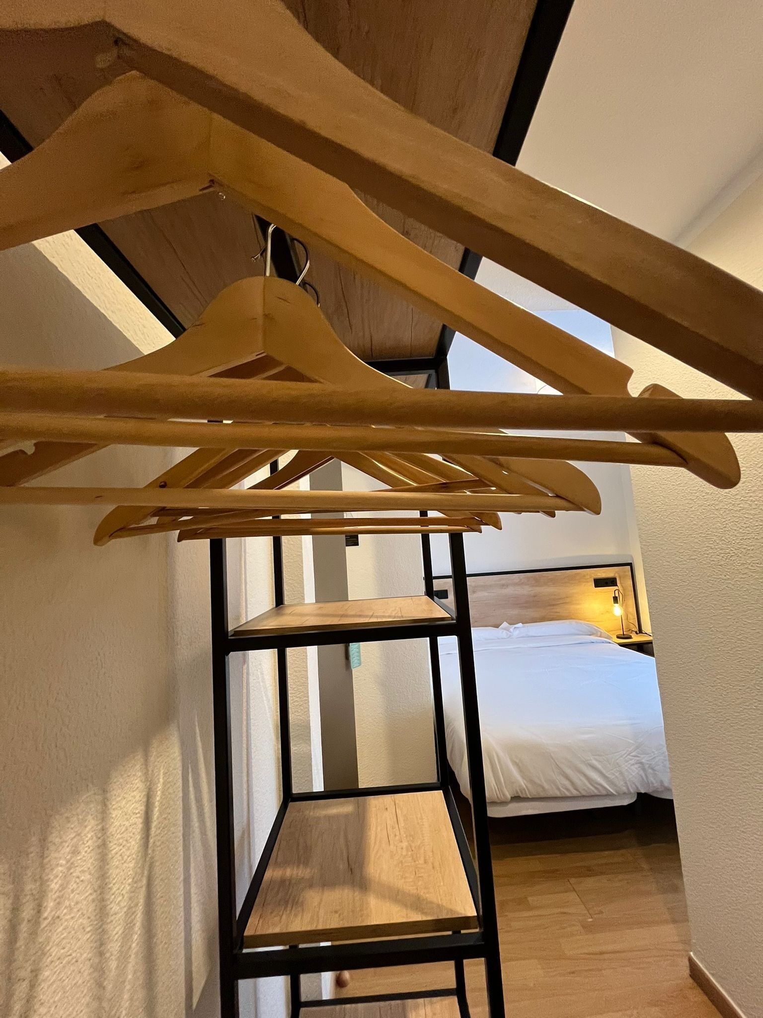 A room with a bed, a wooden hanger rack, and a small wooden table.