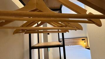 A room with a bed, a wooden hanger rack, and a small wooden table.