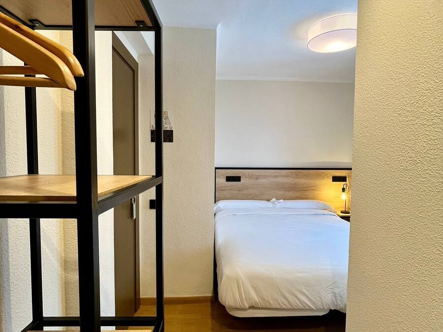 A compact hotel room with a bunk bed, a single bed, a wooden floor, and a ceiling light.