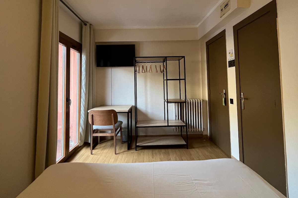 Una habitación de hotel con cama, escritorio, silla, televisor montado en la pared y radiador.