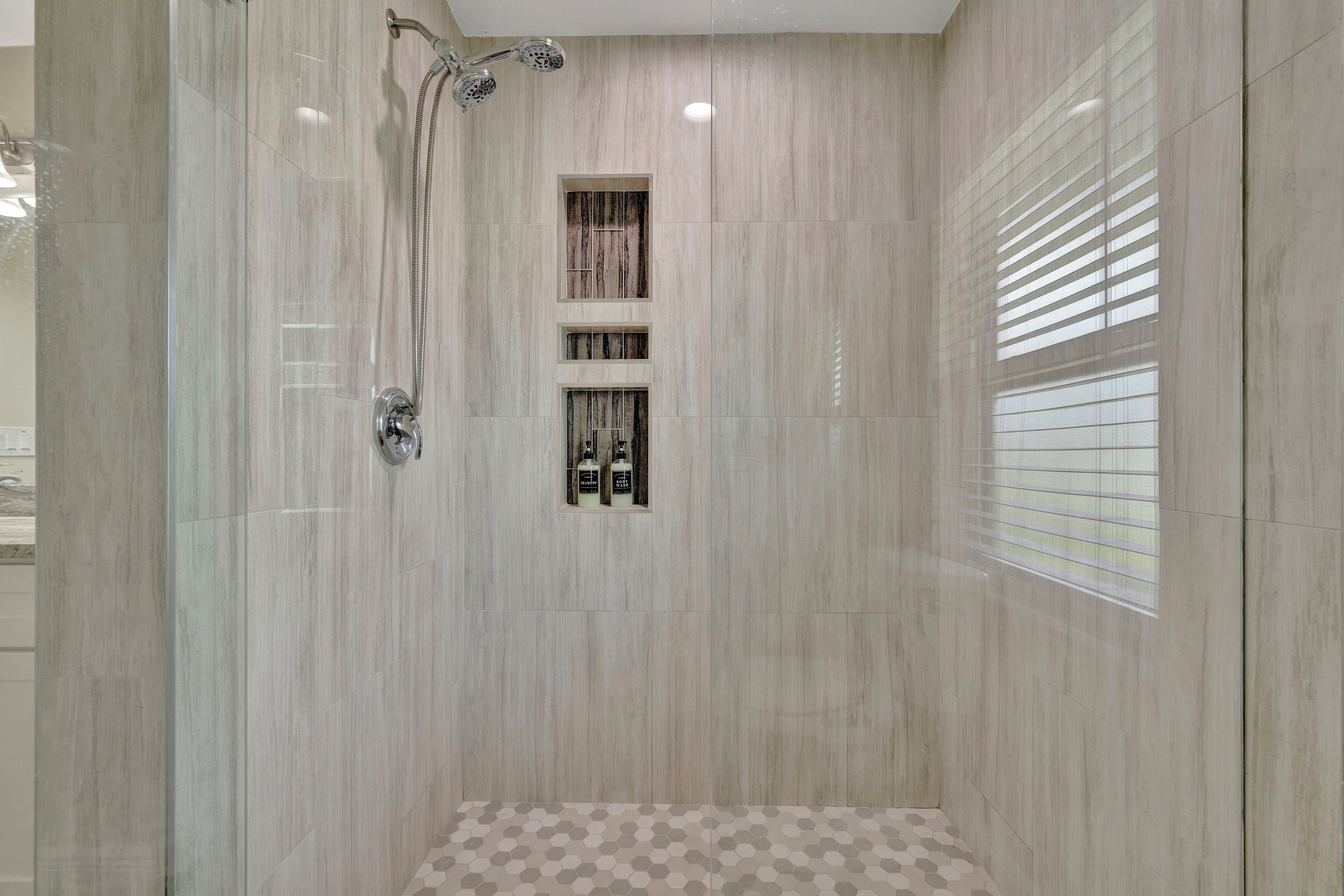 A modern bathroom with a glass-enclosed shower, a built-in shelf with toiletries, and a patterned floor.