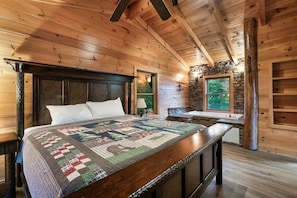 Ein Schlafzimmer in einer Holzhütte mit einem Bett, einer Patchworkdecke, einer Steinwand und einem Fenster.
