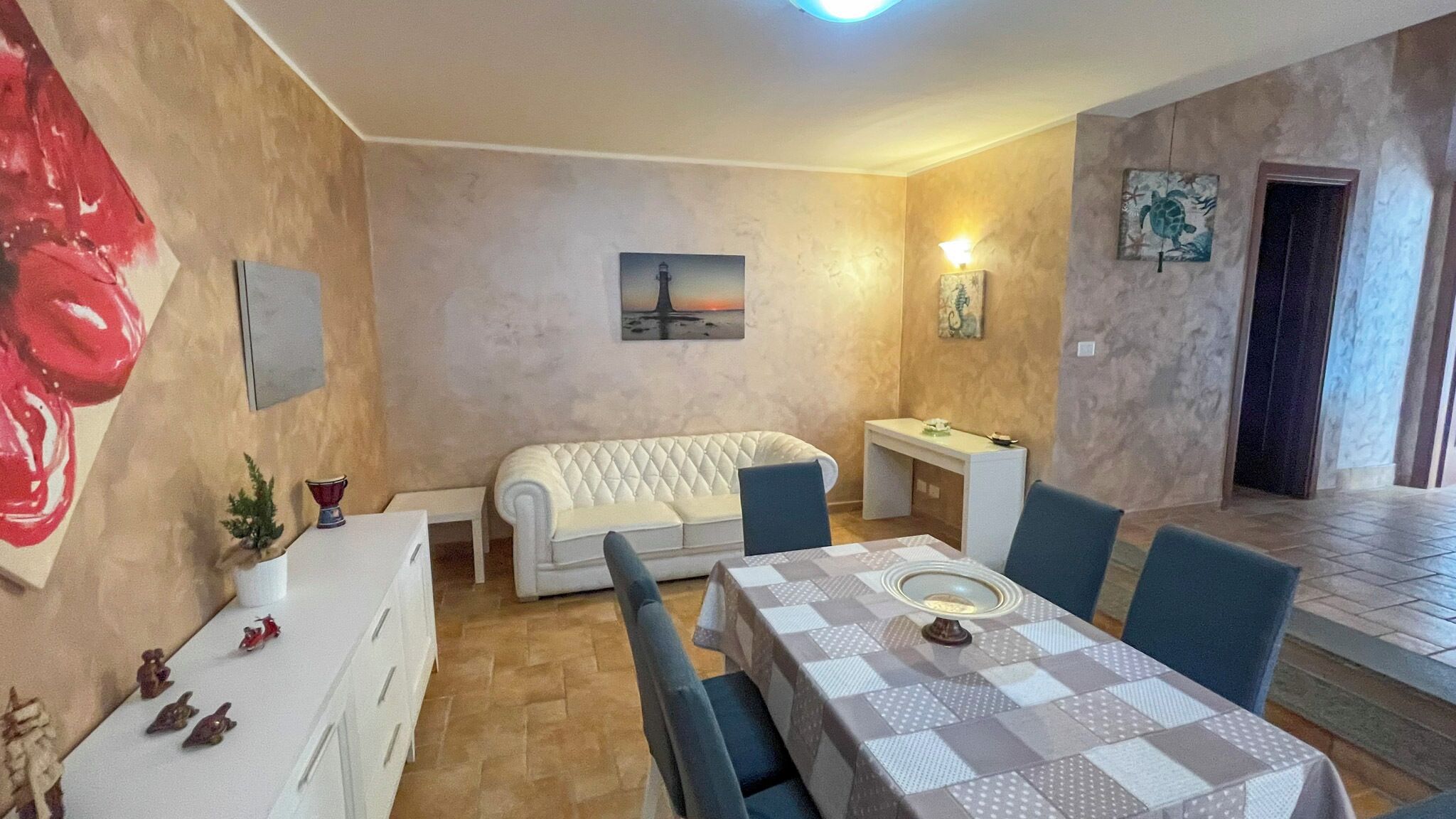 A dining area with a table set for four, a white sofa, and a small side table with decorative items.