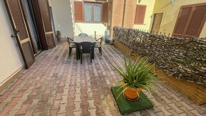 Un patio con una mesa y sillas, una planta en maceta y un muro decorativo.