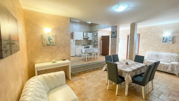 Un salón acogedor con un sofá blanco, una mesa de comedor con sillas y una cocina al fondo.