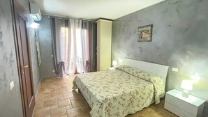 Un dormitorio con cama, mesita de noche, reloj de pared, ventana con cortinas y puerta.