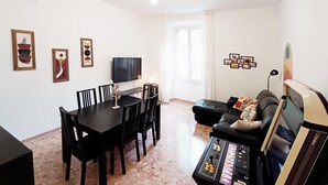 Ein Wohnzimmer mit Esstisch, Stühlen, einer Couch und einer Spielkonsole.