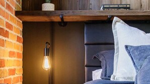 Ett sovrum med en tegelvägg, en sänggavel i trä, ett nattduksbord med en lampa och en säng med blått sänglinne.