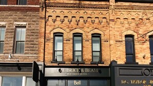 En byggnad med en fasad av tegel, en skylt med texten ”The Brick & Beam Boutique Hotel” och en väl synlig butiksfasad med en klocka ovanför ingången.