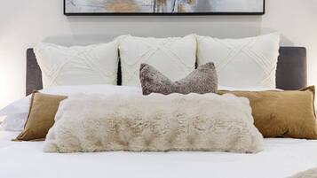 A bed with white and brown pillows, a fluffy white throw, and a dark headboard.