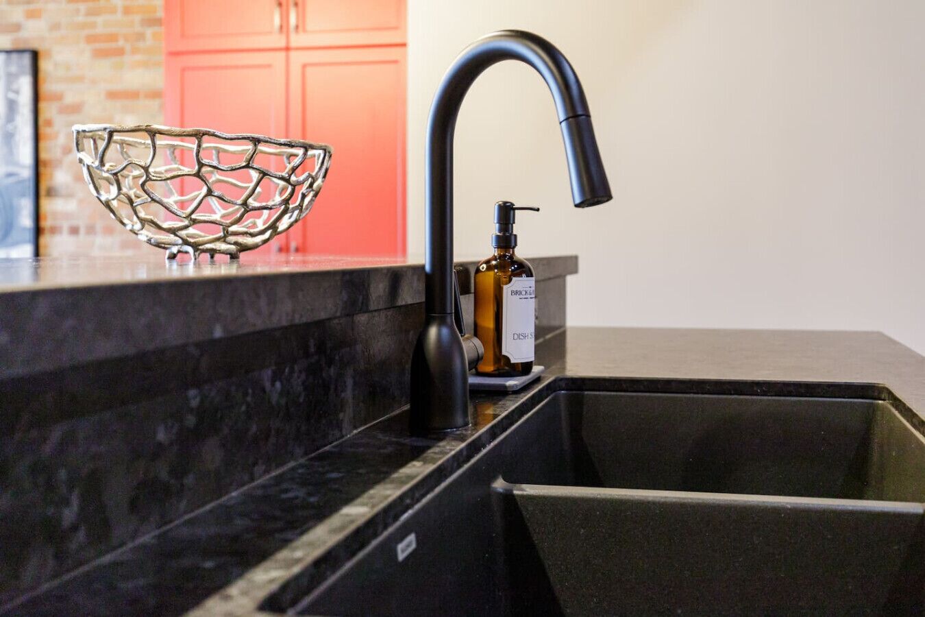 A kitchen with a black sink, a bottle of dish soap, and a decorative glass bowl on the counter.