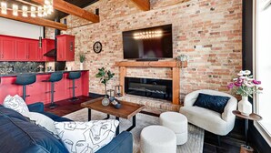 Una sala de estar moderna con chimenea de ladrillo, armarios de cocina rojos y un televisor grande montado encima.