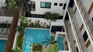 Ein Pool auf dem Dach mit Liegestühlen und Palmen, umgeben von einem Hochhaus.