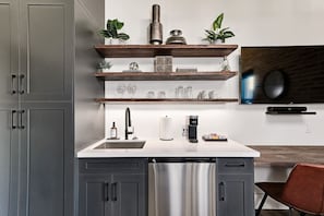 A modern kitchen with grey cabinets, a stainless steel refrigerator, a coffee maker, and wooden shelves with decorative items. - Chic Studio for Two, Steps from Everything (Collingwood)