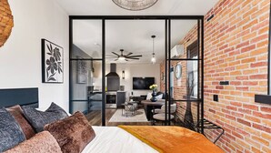 A modern hotel room with a large bed, a dining area, and a kitchen visible through a glass partition.
