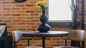 A brick wall with a large analog clock, a round table with two chairs, and a vase with yellow flowers.
