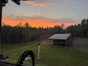 A rural landscape with a wooden cabin, a grassy field, and a forest in the background. - Fantastic 4-bedroom home with direct snowmobile and atv access (Colebrook)