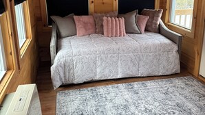 Un dormitorio de cabaña acogedor con techo de madera, cama con ropa de cama floral y un ventanal con persianas.