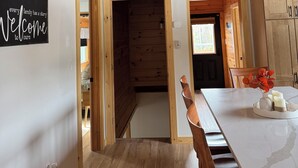 Amplia habitación tipo loft con techo alto, vigas de madera, zona de comedor con mesa de mármol y cocina a la vista a través de un vano abierto.